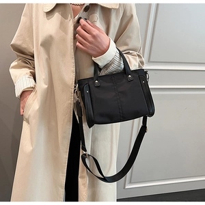 Detalle del bolso tote de nailon negro con asas de cuero y correa ancha sobre modelo