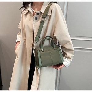 Detalle de bolso bandolera verde oliva en nailon y cuero con gabardina beige en modelo