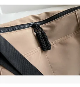 Detail of smooth black double zipper and woven rope pulls on khaki nylon tote bag