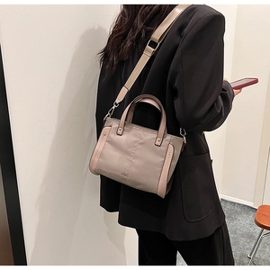 Detalle de bolso tote de nailon topo con correa ancha en una modelo con chaqueta negra