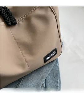 Detail of khaki nylon tote bag showing woven drawstrings and logo patch on fabric