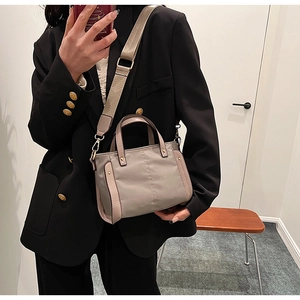 Detalle de bolso mensajero gris con correa ancha de tela y herrajes dorados