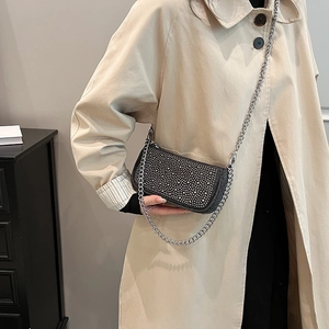 Elegant black crossbody bag with silver studs and chain strap worn by a model in a trench coat