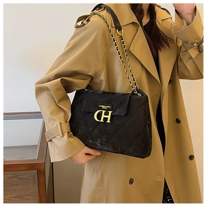Détail d'un sac bandoulière en velours matelassé noir avec logo doré sur un trench