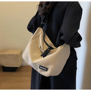 Close-up of beige nylon crossbody bag featuring black logo tag and rope zipper detail