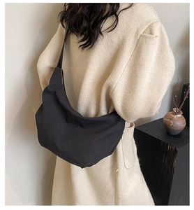 Model wearing a large black matte nylon crescent bag with textured shoulder strap