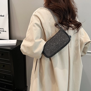 Elegant black crystal baguette bag with silver chain worn over a beige trench coat