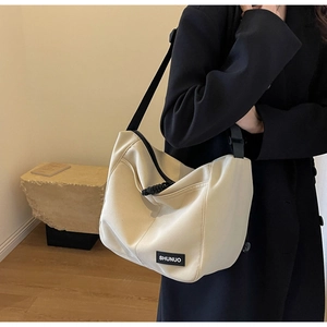 Side view of beige nylon tote bag with black strap and brand label on a model