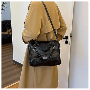 Dettaglio di una borsa nera lucida con fibbie metalliche argentate e tracolla sottile