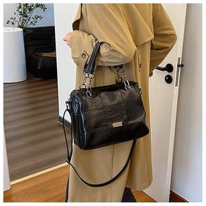 Dettaglio di una borsa nera trapuntata con tracolla su un trench color kaki