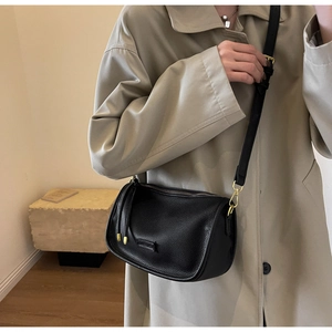 Detail view of black lychee grain Boston bag with gold hardware worn on trench coat