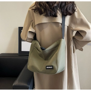 Detail of olive green canvas hobo bag with black brand tag and wide shoulder strap