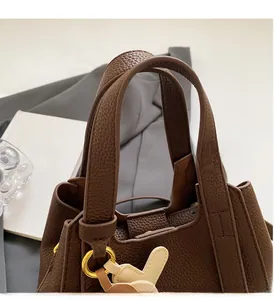 Detail of comfortable brown lychee leather handles and golden metal rings on a bucket bag