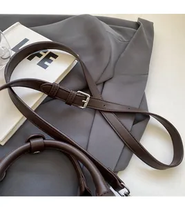 Detail of adjustable dark brown leather strap and silver buckle on a crossbody bag