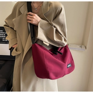 Close-up of wine red nylon tote bag with black logo tag and adjustable shoulder strap