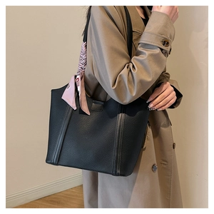 Detail of black pebbled leather tote bag with decorative silk scarf on trench coat model