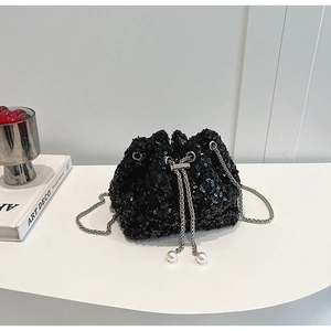Détail d'un sac seau noir à paillettes avec chaîne argentée et accents de perles blanches