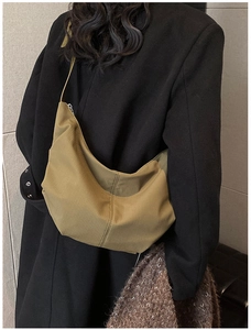 Detail of olive crescent crossbody bag with textured fabric shown on black wool coat
