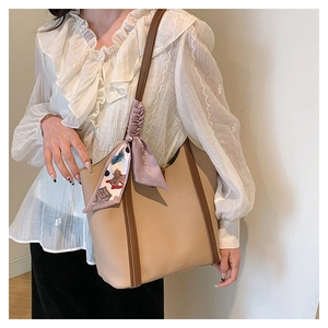 Detail of a large khaki leather tote bag with brown straps and a decorative silk scarf