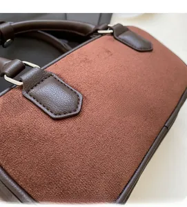 Close-up of contrast brown leather and matte suede stitching on a small square handbag