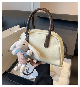 Detail of cream Boston bag with plush bunny charm and textured faux leather finish