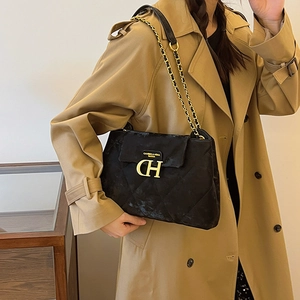 Sac bandoulière matelassé noir avec chaîne dorée porté sur un trench-coat classique