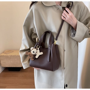 Detail of dark brown pebble leather bucket bag with cute bear charm and gold hardware