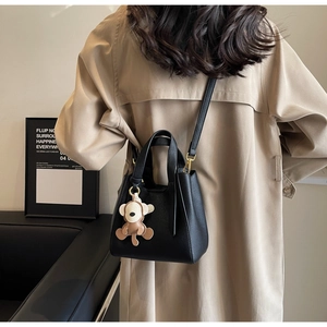 Detail of black lychee leather bucket bag with monkey charm worn with beige trench coat