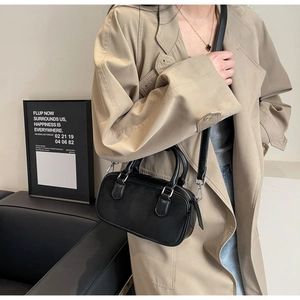 Detail of black suede patchwork crossbody bag with silver hardware on a trench coat