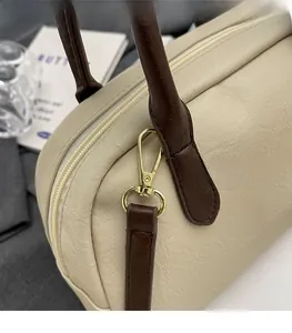 Close-up of polished gold-tone hardware and lychee texture on cream Boston bag