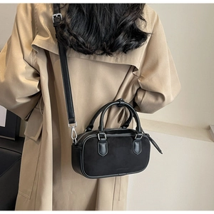 Detail shot of a black mini crossbody bag worn with a khaki trench coat for scale