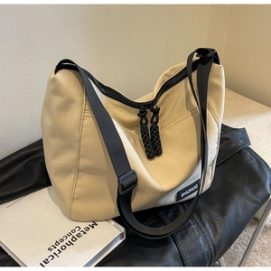 Detail of beige nylon tote bag featuring black woven zippers and branded rectangle label