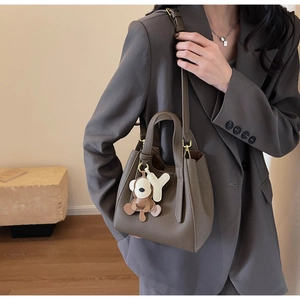 Detail of dark brown leather bucket bag with bear charm and adjustable strap