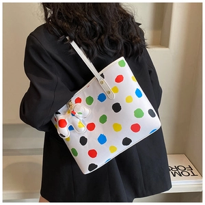 Détail du grand sac cabas blanc à pois multicolores porté sur un blazer noir chic