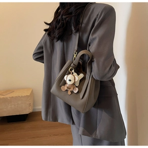Detail of dark brown lychee leather bucket bag with monkey charm on grey suit