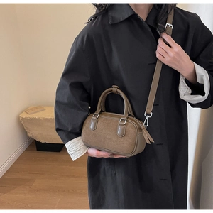 Detail of a brown suede Boston bag featuring dual handles and adjustable shoulder strap