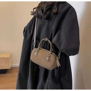 Close-up of brown matte suede Boston bag with smooth leather handles worn with black coat