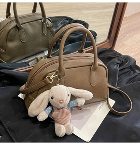 Detail of a brown Boston bag showing leather texture and a cute plush rabbit pendant