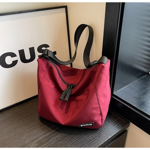 Close-up of burgundy nylon tote bag with black dual zippers and adjustable shoulder strap