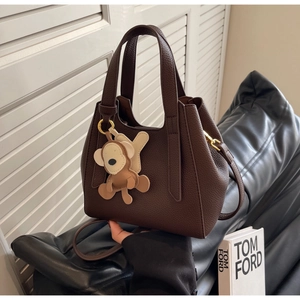 Detail of dark brown pebble leather bucket bag with monkey charm and crossbody strap