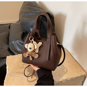 Detail of dark brown leather bucket bag with monkey charm on a stone base