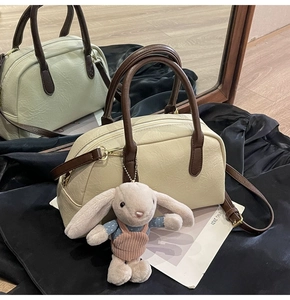 Detail view of cream Boston bag with brown handles and a cute bunny pendant charm