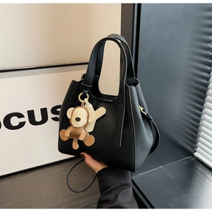 Close-up of black lychee grain bucket bag with adorable monkey charm and dual straps