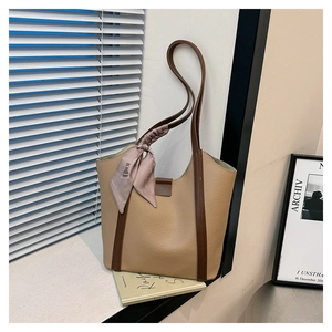 Detail of khaki leather tote bag featuring brown straps and a decorative floral silk scarf