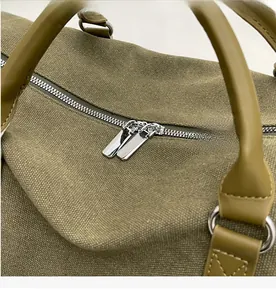 Detail of smooth metal zippers and reinforced faux leather handles on olive canvas bag