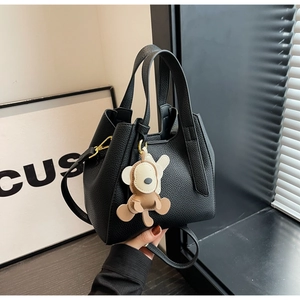 Close-up of black lychee grain leather bucket bag with cute bear charm and strap