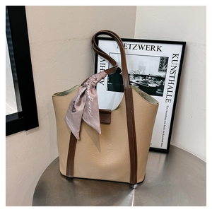 Detail of beige tote bag with brown leather handles and decorative purple silk scarf