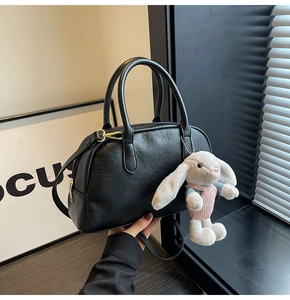 Detail of black faux leather Boston bag with gold zipper and pink plush rabbit charm