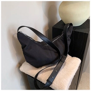 Detail of black nylon dumpling bag with adjustable strap on a soft plush white rug