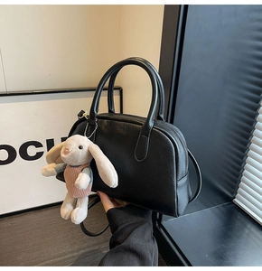 Close-up of black leather Boston bag with a cute rabbit plush charm on dark wood surface